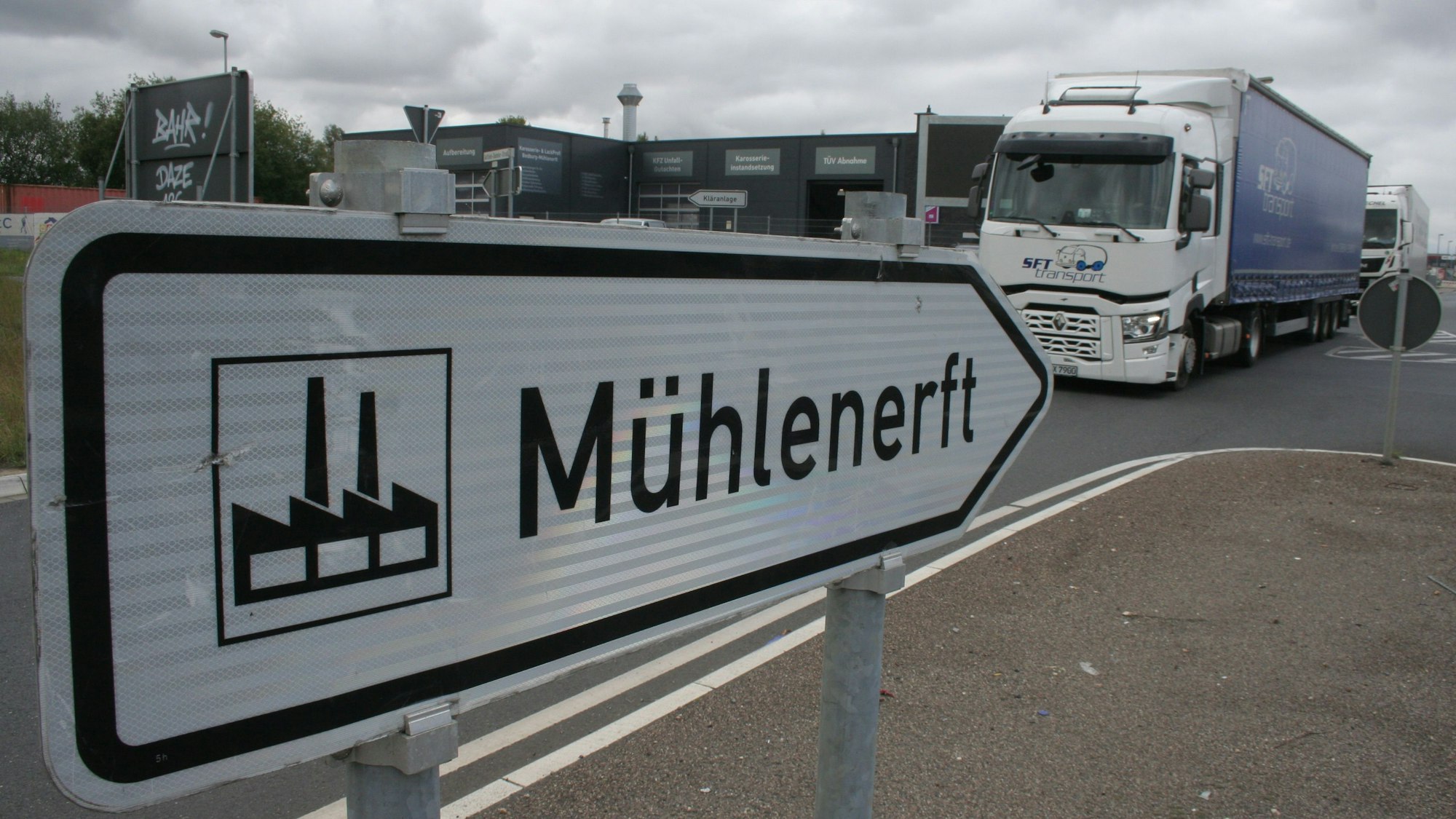 Zu sehen ist ein Straßenschild, das den Weg in das Gewerbegebiet Mühlenerft weist, und ein Lkw.