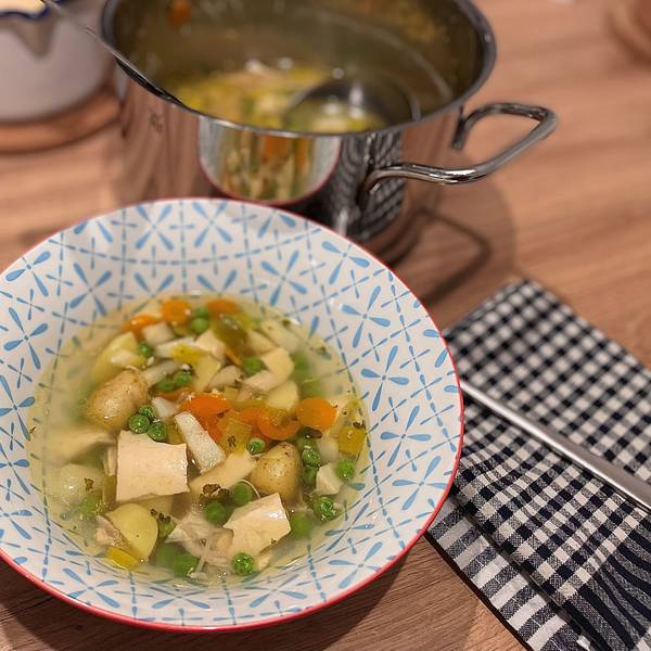 Hühnersuppe in einer Schale, dahinter steht ein Topf.