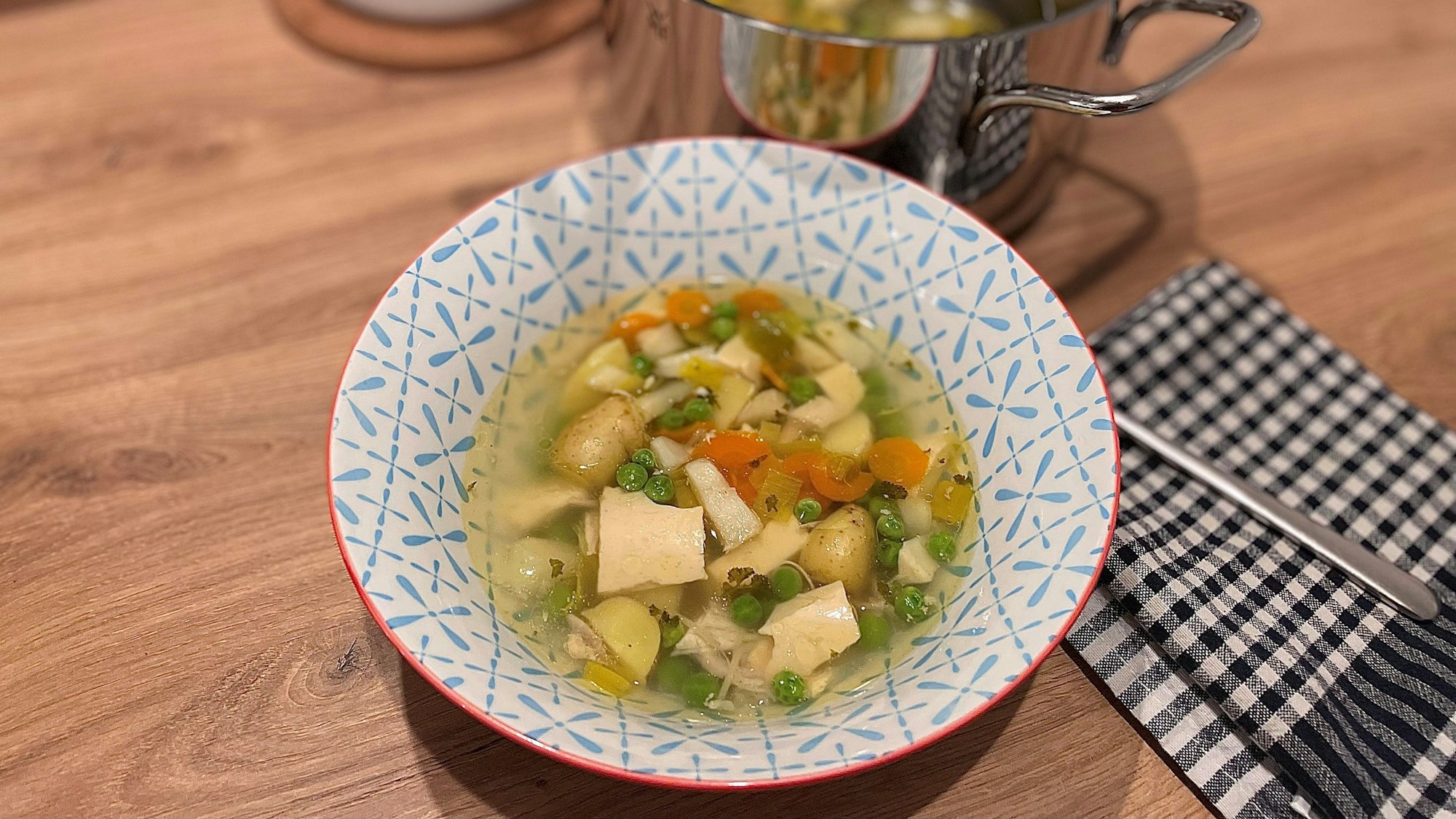 Hühnersuppe in einer Schale, dahinter steht ein Topf.