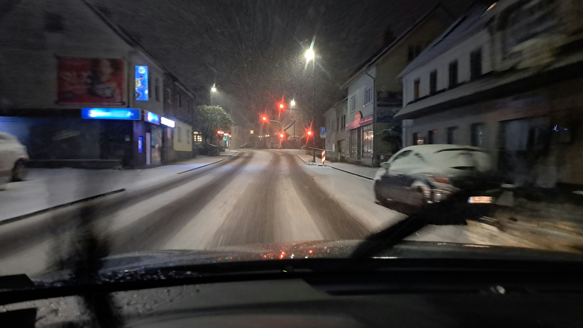Durch die Windschutzscheibe eines Autos ist die verschneite Bensberger Straße in Bergisch Gladbach-Heidkamp zu sehen.