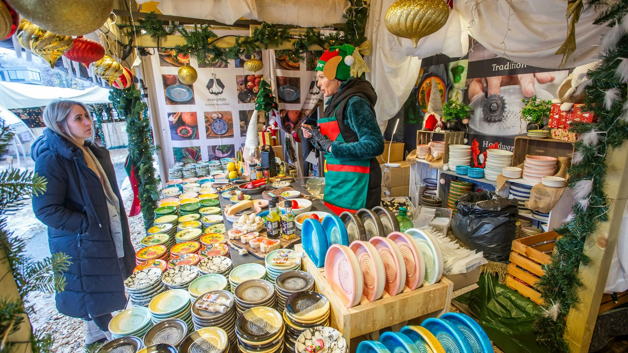 Eine Frau schaut sich bunte Teller an einem Stand auf einem Weihnachtsmarkt an.