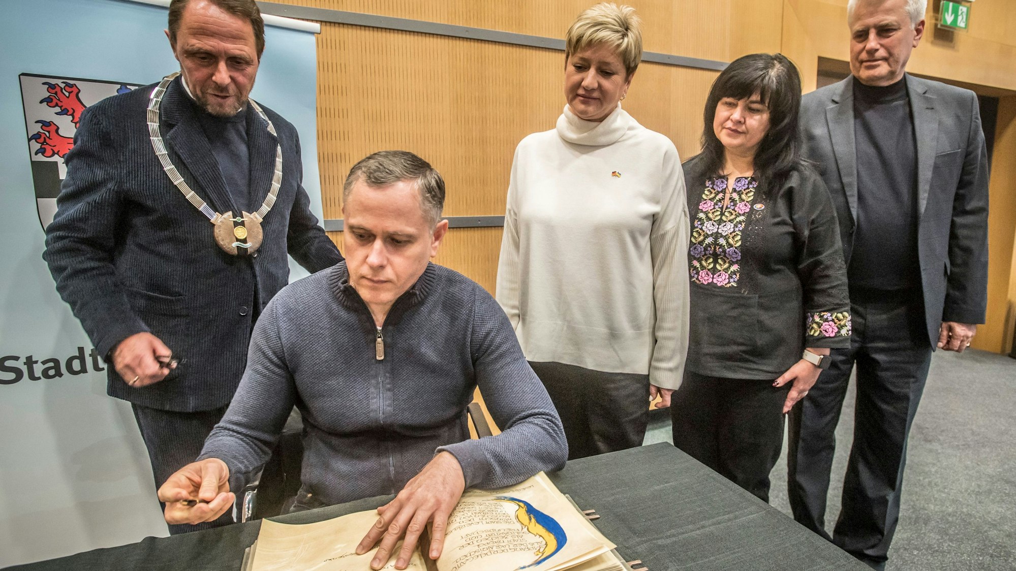 Bürgermeister Oleksandr Saiduk und seine Delegation (rechts) aus Nikopol tragen sich ins Goldene Buch ein. Links Oberbürgermeister Uwe Richrath mit Amtskette.