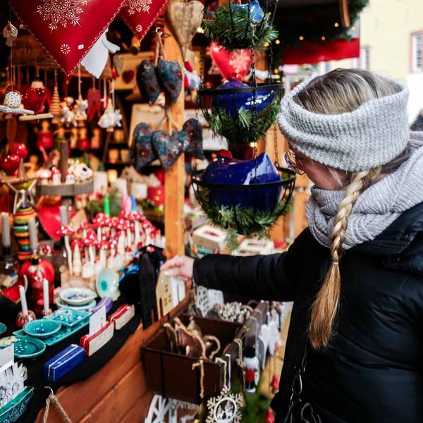 Das Bild zeigt eine Frau, die sich Deko an einer Weihnachtsbude anschaut.