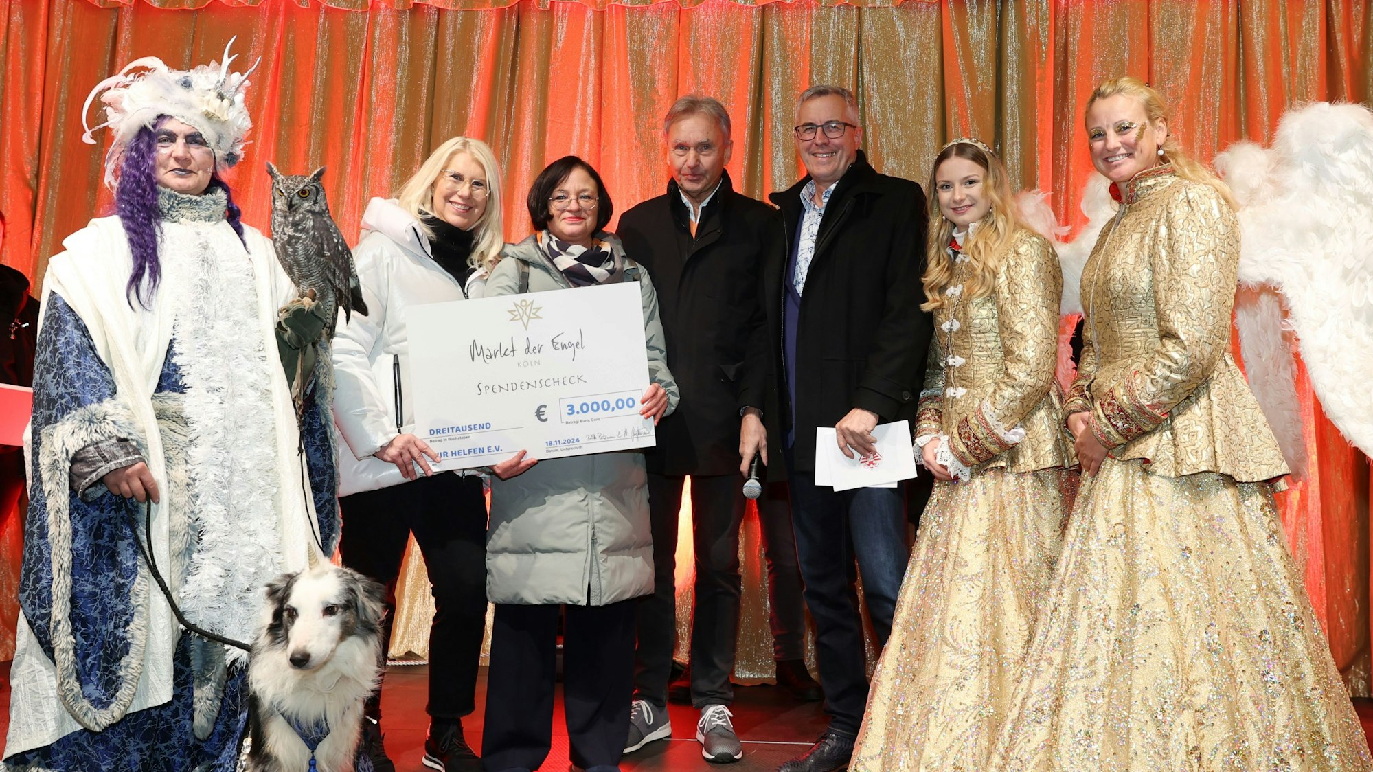 Spendensegen mit Eiskönigin, Engeln und Bürgermeister Andreas Wolter (5. von links): Das „Markt der Engel“-Veranstalter-Ehepaar Britta und Herbert Putzmann überreichen Caroline Kron von „wir helfen“ einen symbolischen Scheck in Höhe von 3000 Euro.