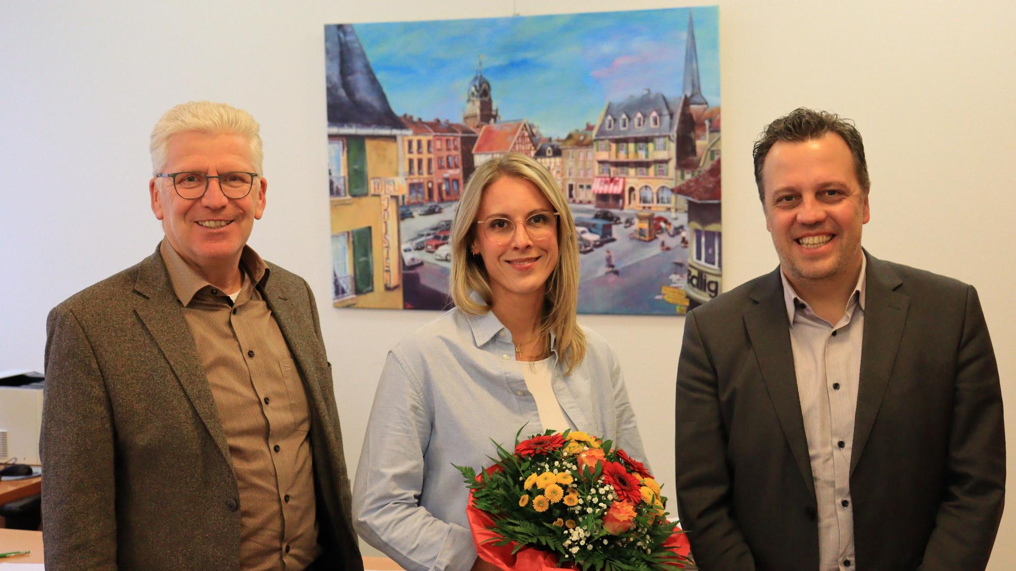 Jennifer Corsten hält einen Blumenstrauß in der Hand. Alfred Jaax und Sacha Reichelt stehen links und rechts neben ihr.