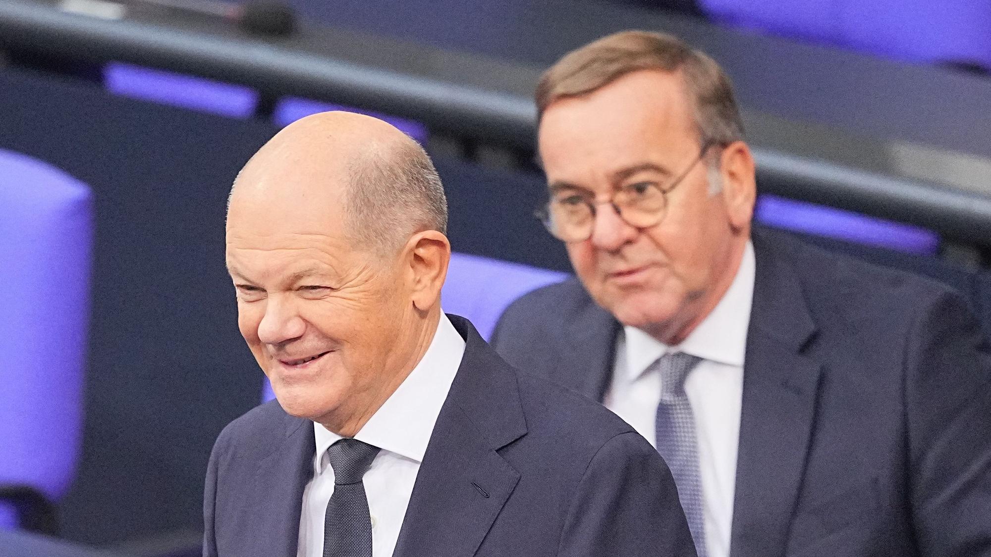Bundeskanzler Olaf Scholz (SPD) steht lächelnd im Plenum des Bundestags vor Boris Pistorius (SPD), Bundesminister der Verteidigung.