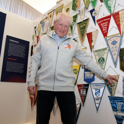 Karl Höver steht vor einer Sammlung zahlreicher Handball-Wimpel und zeigt auf eines des VfL Gummersbach.