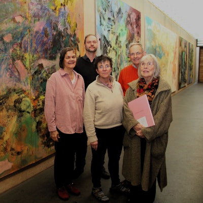 Fünf Personen stehen vor mehreren großen Gemälden.