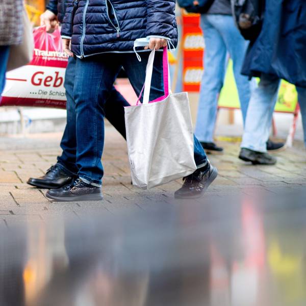 Menschen gehen mit Einkaufstaschen durch die Fußgängerzone einer Innenstadt.