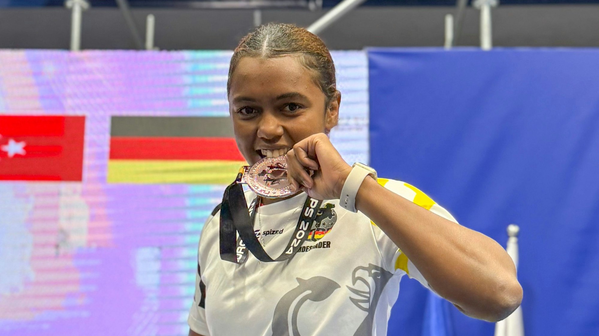 Claudia Toly Henri beißt in ihre Medaille und lächelt.