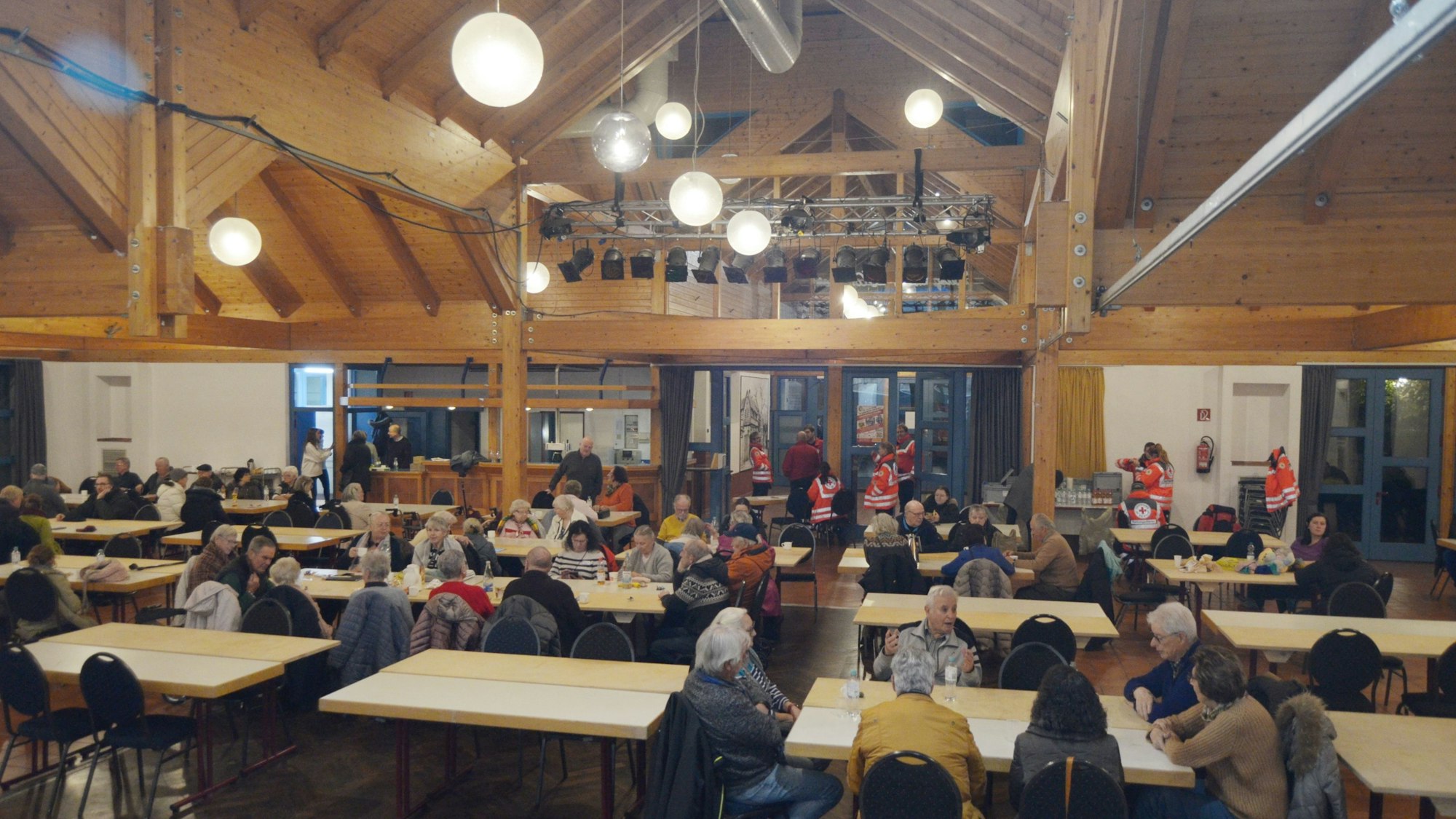 In der beleuchteten Bürgerhalle Kommern sitzen Menschen an Tischen.