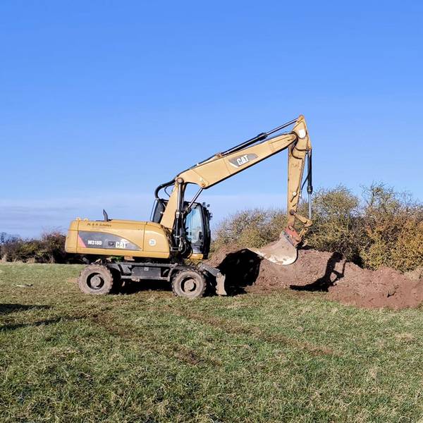 Ein Bagger steht auf einem Feld neben einem Erdhaufen.