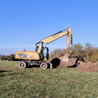 Ein Bagger steht auf einem Feld neben einem Erdhaufen.