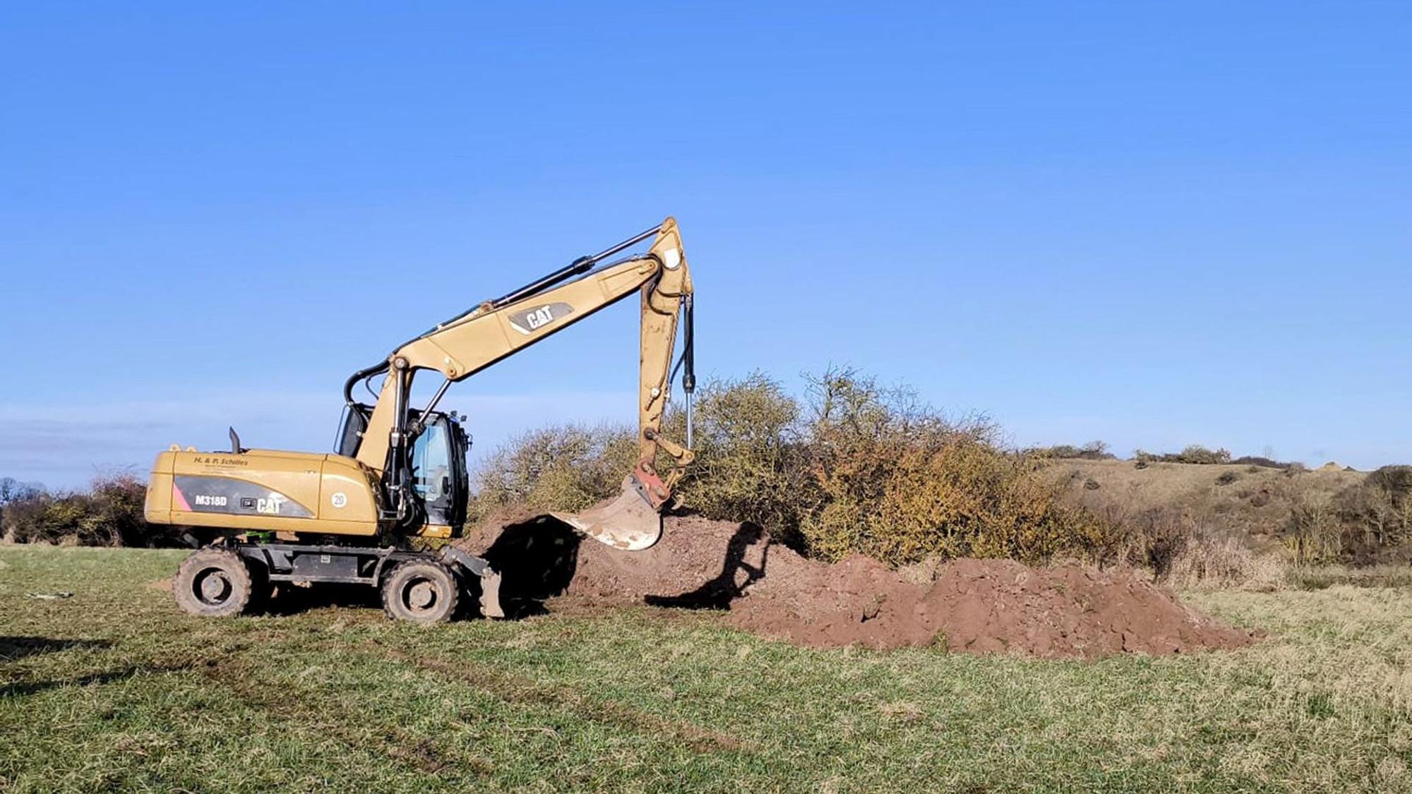 Ein Bagger steht auf einem Feld neben einem Erdhaufen.