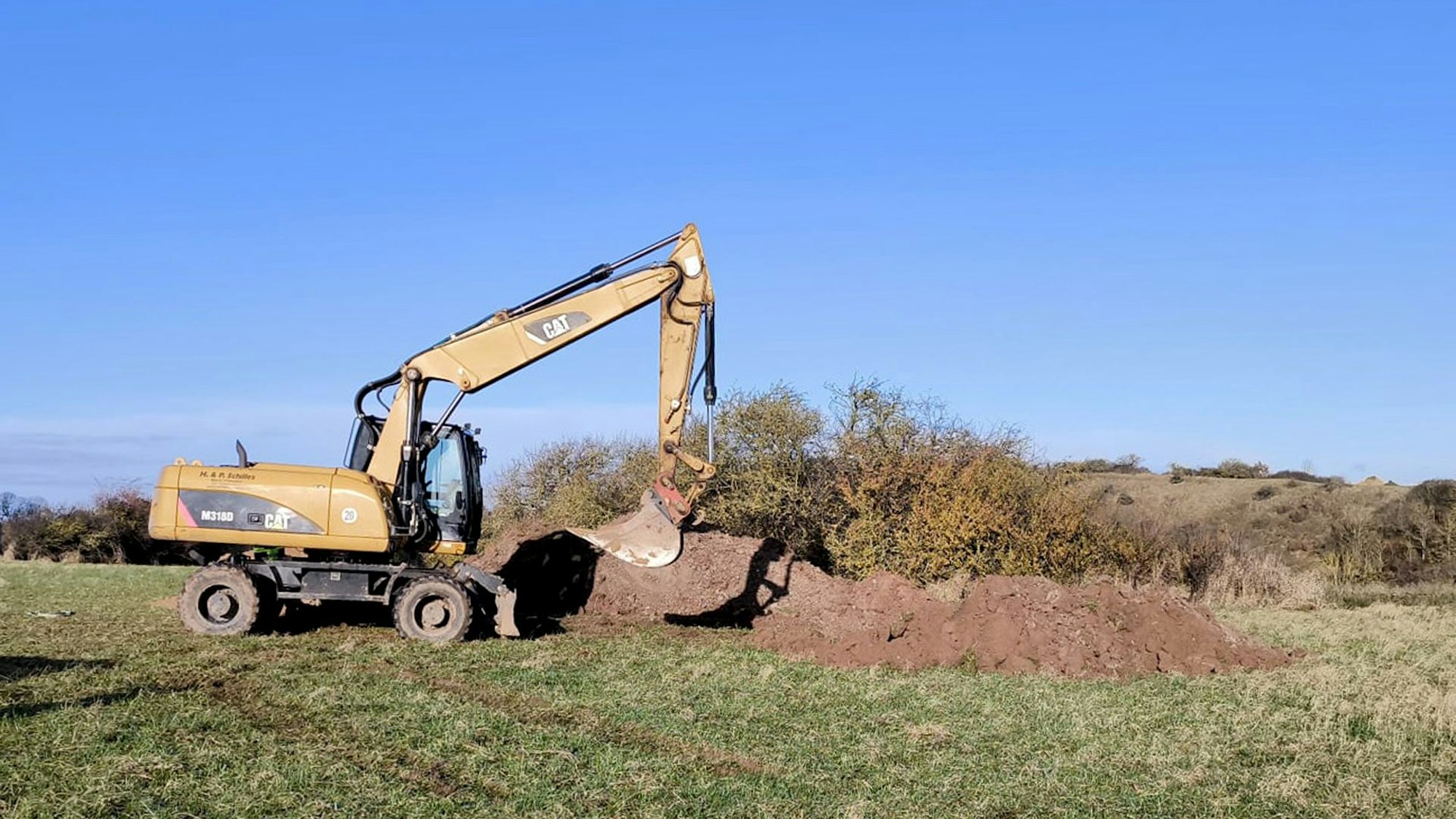 Ein Bagger steht auf einem Feld neben einem Erdhaufen.