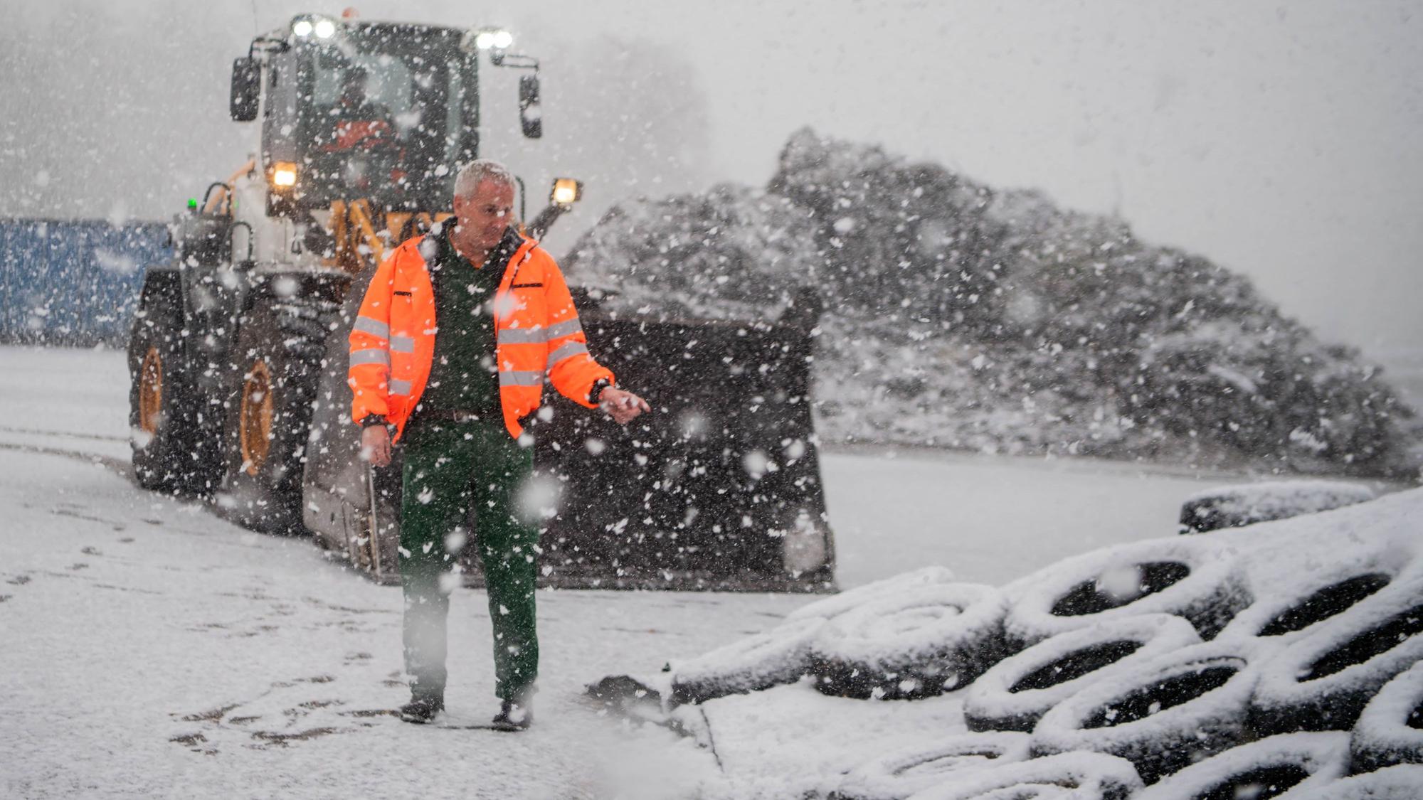 Ein Mann in Warnweste steht draußen neben Reifen, während es schneit.