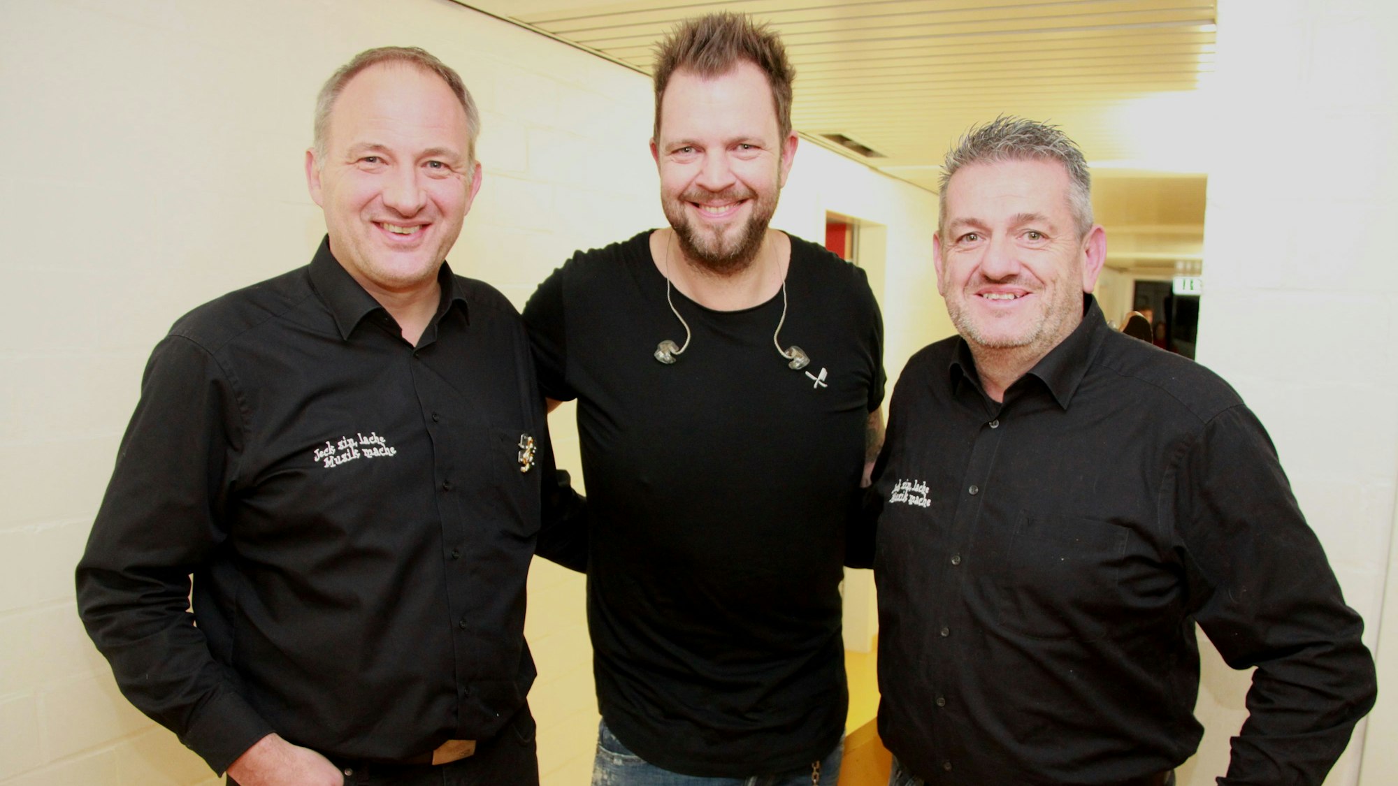 Die drei Mann stehen eingehakt nebeneinander.