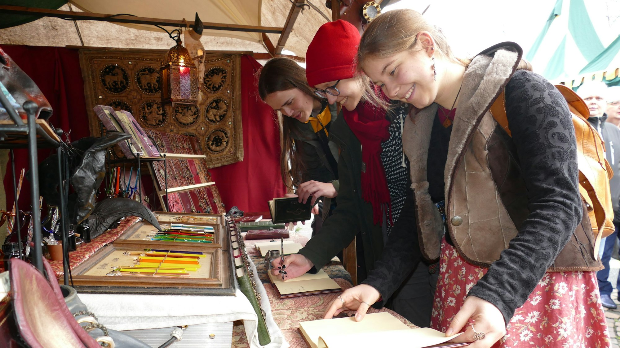 Drei junge Leute beugen sich an einem Stand über Stifte und Papiere.