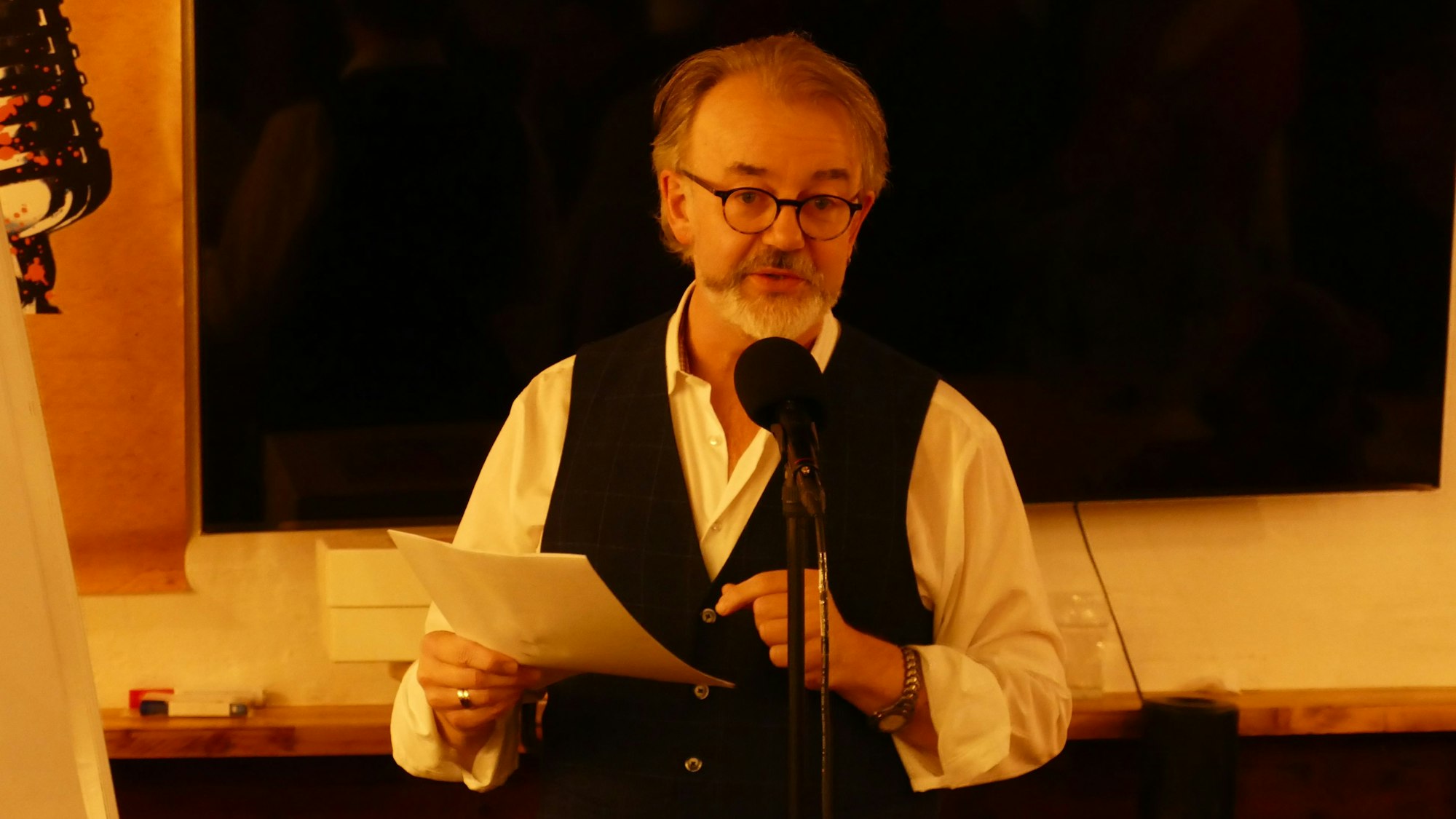 Ein Mann steht am Mikrofon, er hält ein Blatt Papier in der Hand.