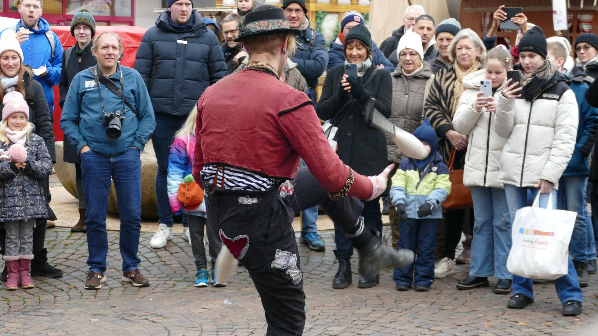 Ein Mann jongliert mit Kegeln, viele Zuschauer stehen im Halbkreis um ihn herum.