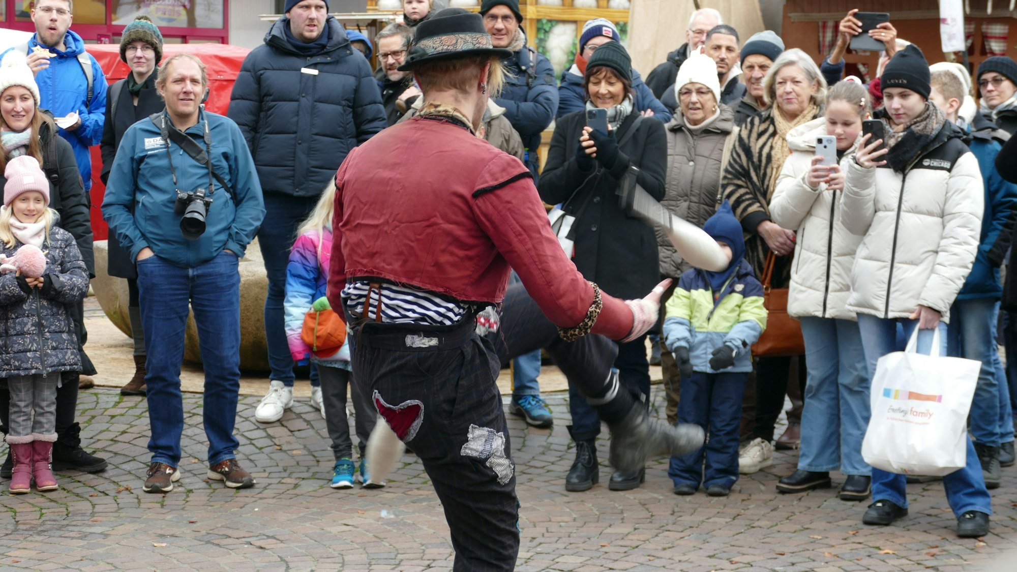 Ein Mann jongliert mit Kegeln, viele Zuschauer stehen im Halbkreis um ihn herum.