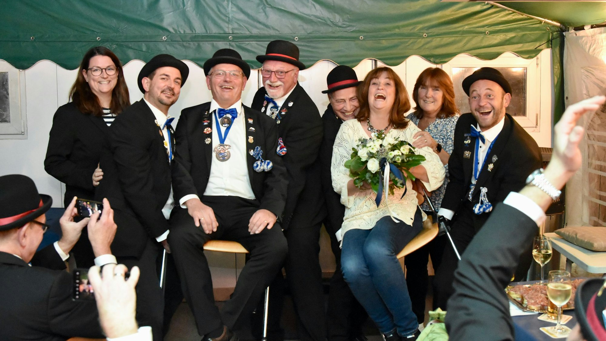 Ein Mann und eine Frau werden von Männern in schwarzen Anzügen und Melonen in die Höhe gehoben.