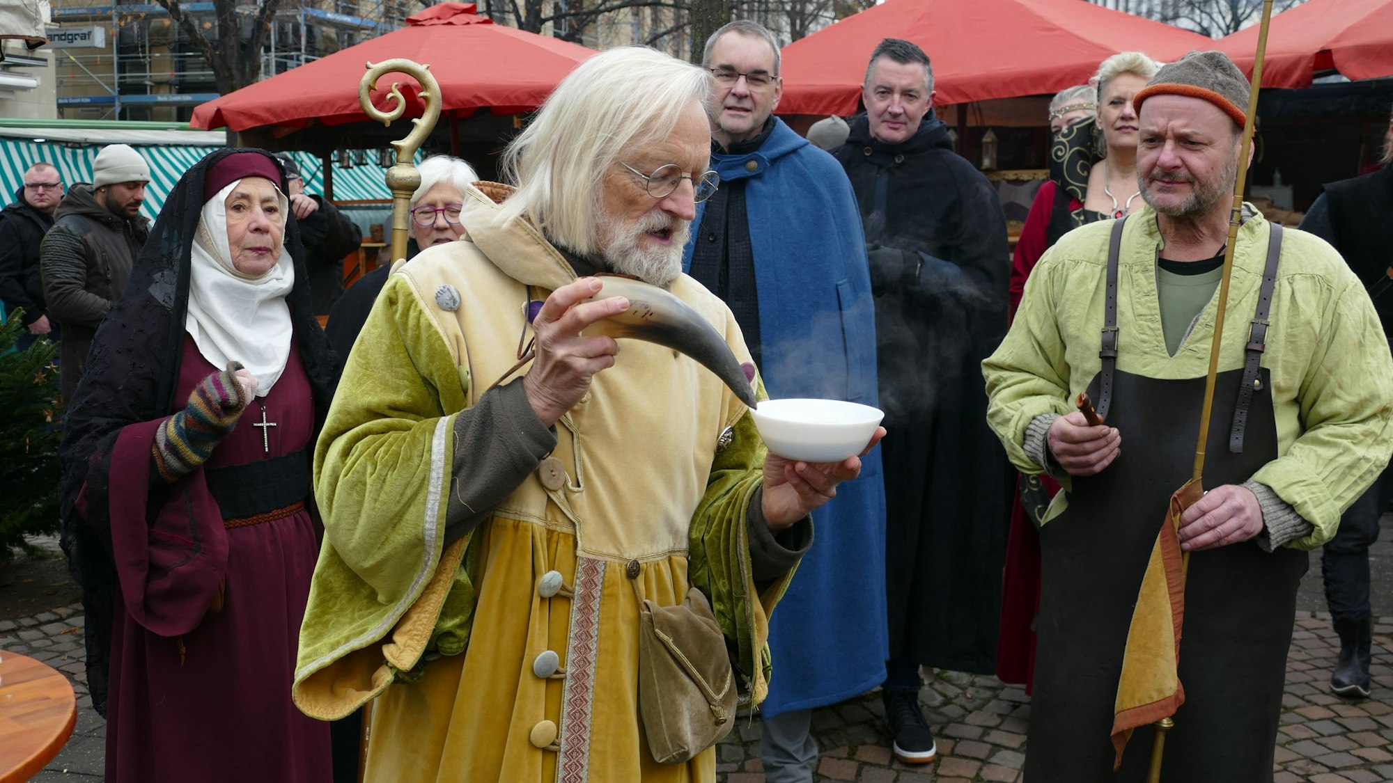 Ein Mann im mitzttelalterlichen Gewand stippt ein Kuhhorn in eine Suppenschüssel.