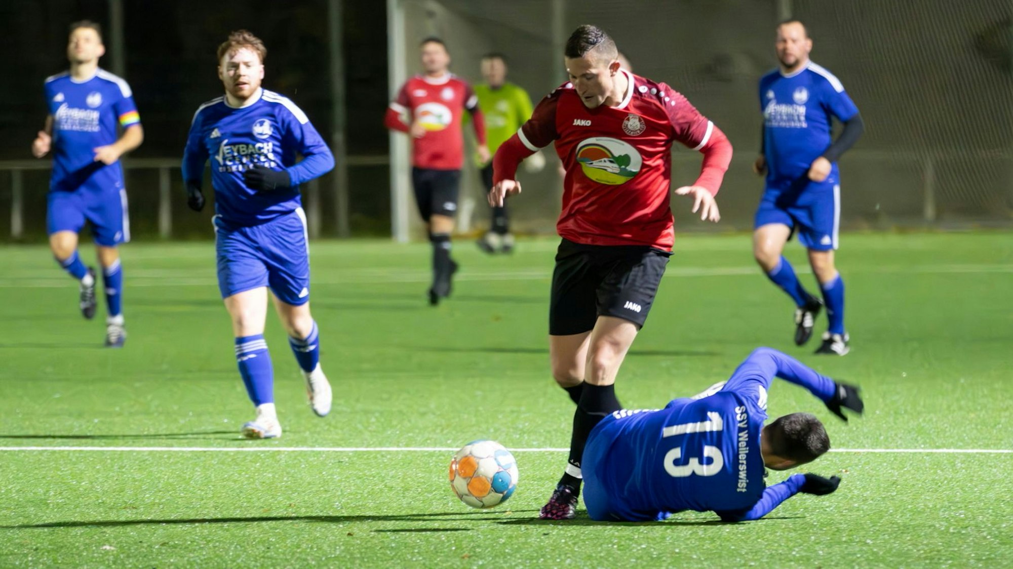 Ein Fußballer legt den Ball an einem auf dem Boden liegenden Gegner vorbei.