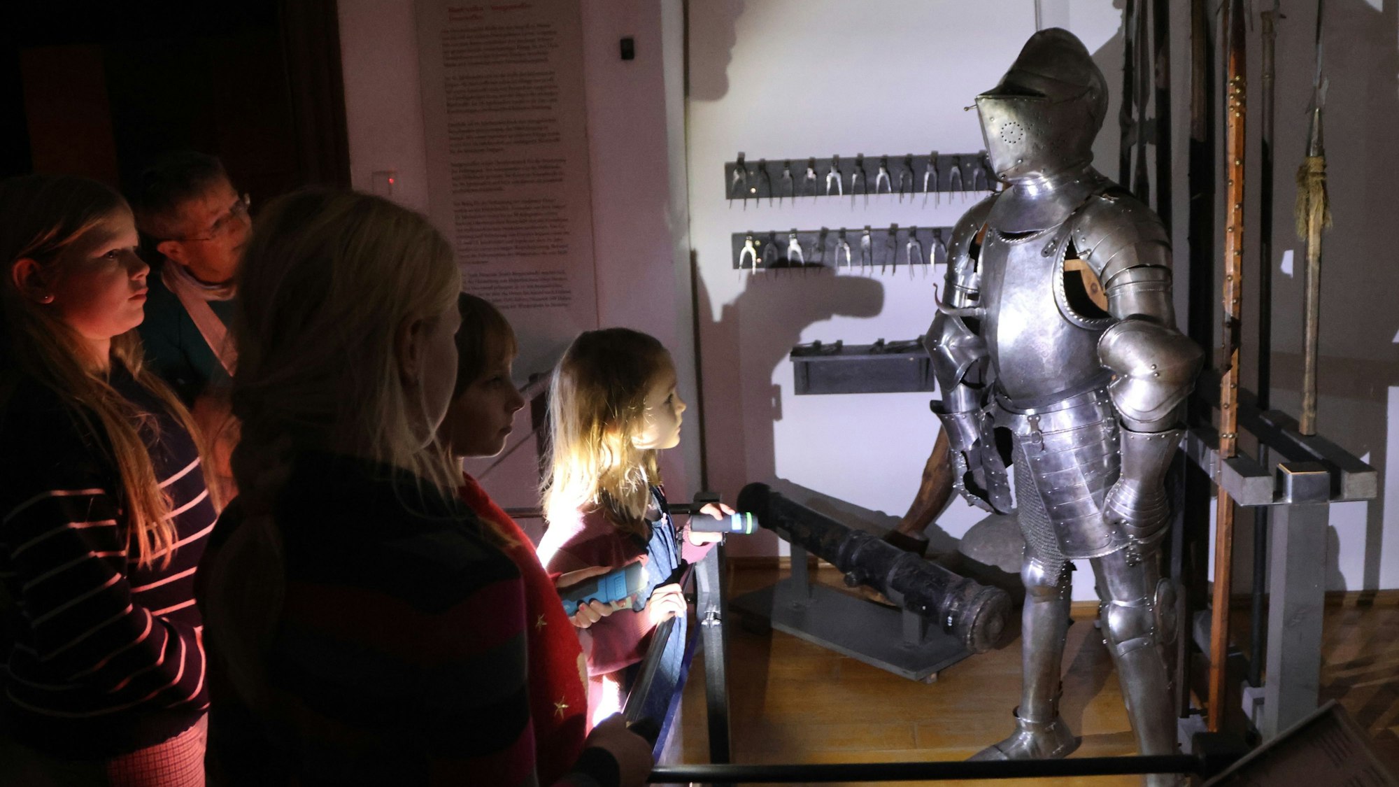 Kinder sehen eine Ritterrüstung im Schein ihrer Taschenlampen.