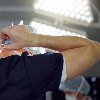 Ein Chirurg bindet sich eine Maske um, er ist nur von hinten zu sehen.