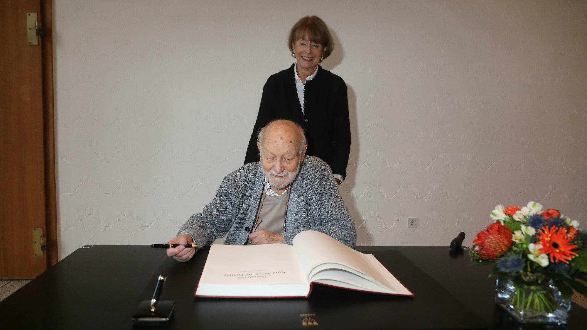 Kurt Marx trägt sich in das Gästebuch der Stadt Köln ein. Henriette Reker steht hinter ihm.