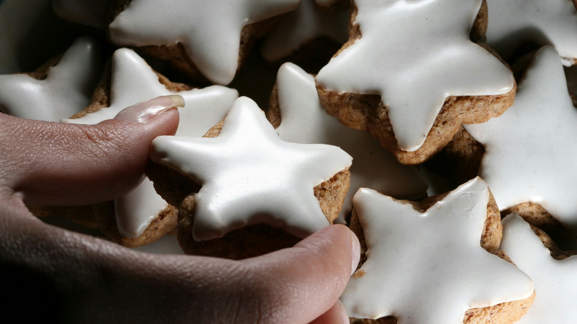 Eine junge Frau nimmt sich einen Zimtstern von einem Teller.