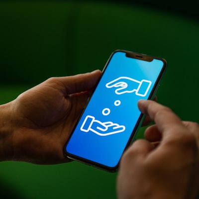 Ein Mann hält ein Handy in den Händen. Auf dem Display sind zwei Hände zu sehen, die sich Geld geben.