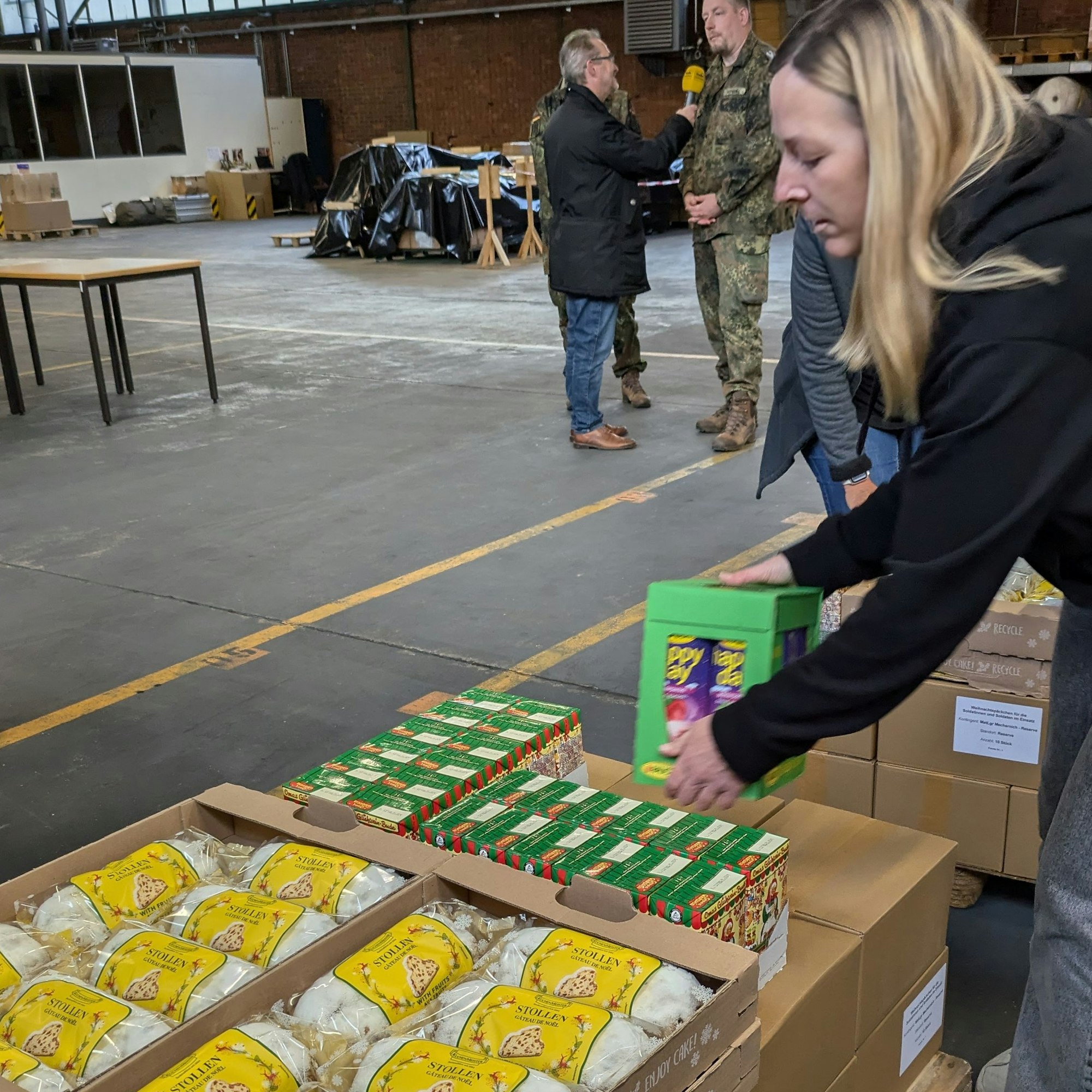 Eine Zivil-Beschäftigte schnappt sich ein Paket mit Saft, um den Inhalt in die Präsente zu stecken. Der Stollen liegt auch schon bereit.