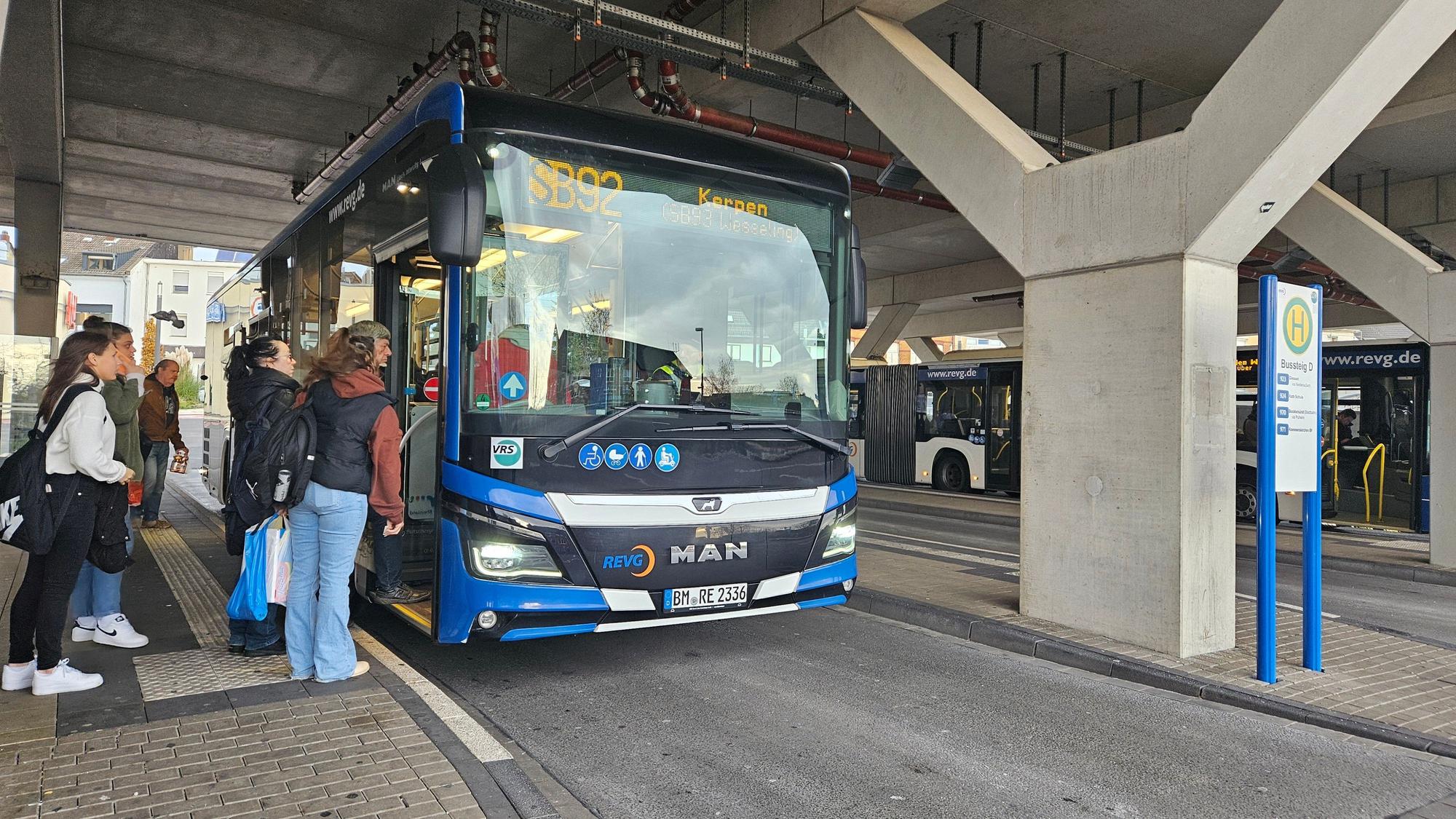 Ein Bus steht an einer Haltestelle, Fahrgäste steigen zu.