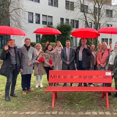 Das Bild zeigt die Initiatoren, die vor dem Amtsgericht in Euskirchen hinter einer roten Bank posieren.