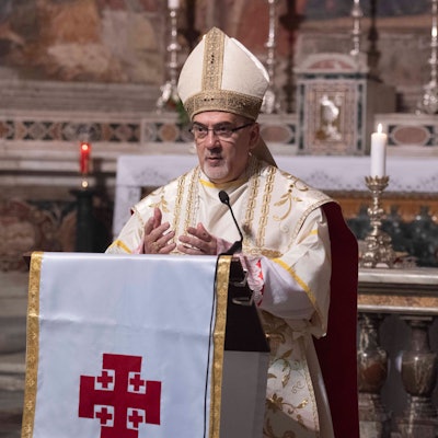 Zu sehen ist Pierbattista Pizzaballa in der Vorderansicht in einer Kirche vor einem Rednerpult in geistlicher Kleidung.