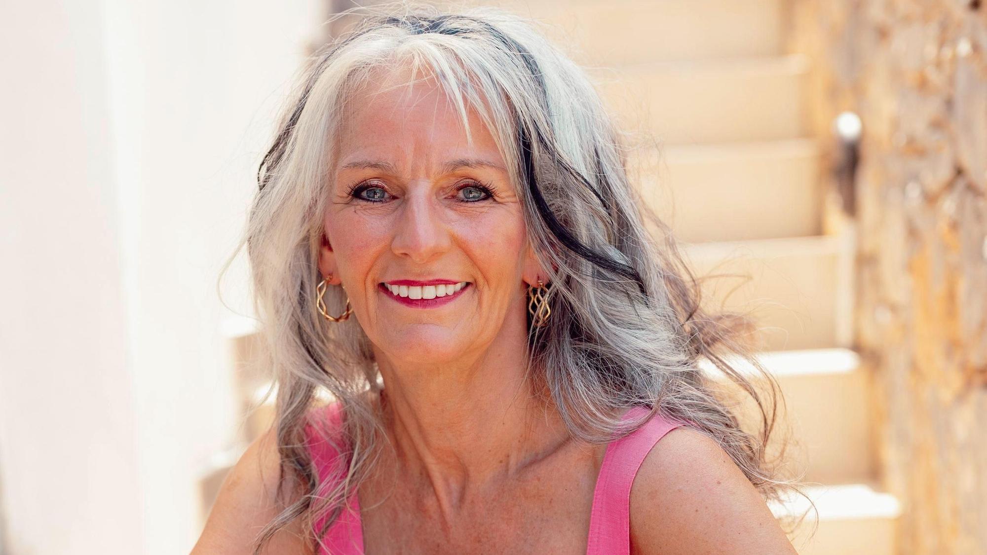 Sabine aus Troisdorf ist dreifache Mutter und eine von 18 Kandidatinnen der RTL-Datingshow „Golden Bachelor“. Sie schaut auf dieser Fotografie lächelnd in die Kamera, sitzt dabei auf einer Treppe.