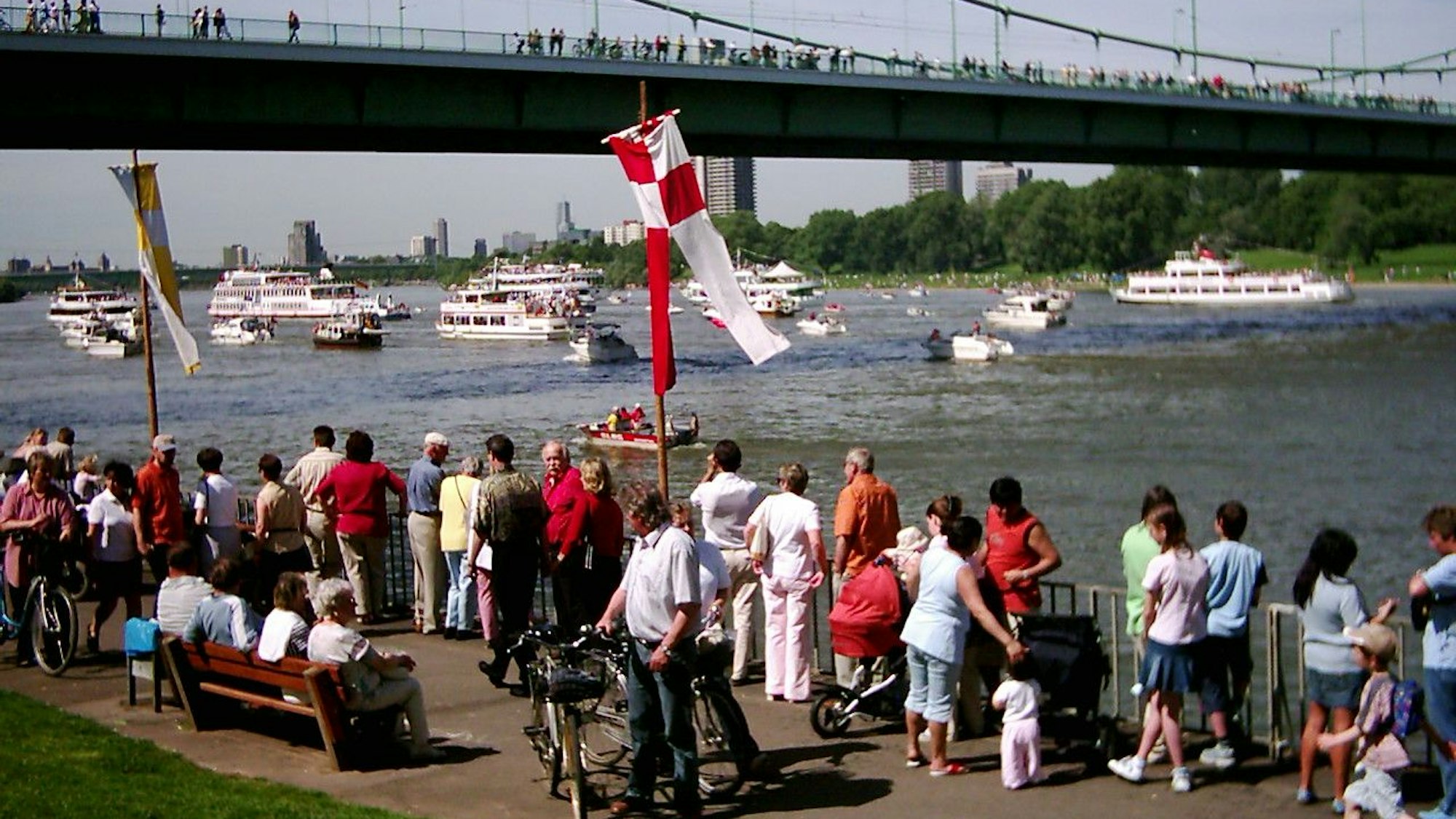 Menschen stehen am Rheinufer und schauen auf vorbeifahrende Schiffe.