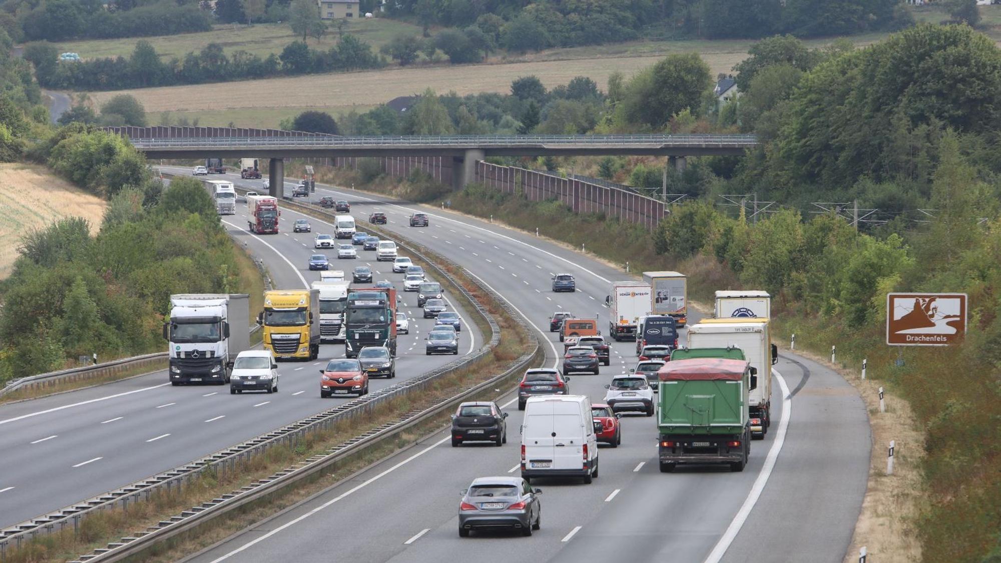 Pkw und Lkw auf einer sechsspurigen Autobahn, ein Schild am Fahrbahnrand weist auf den Drachenfels hin.