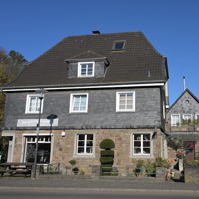 Ein bergisches Fachwerkhaus mit Ladenlokal, dahinter ein Kirchturm.