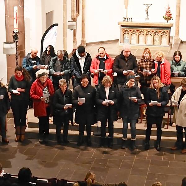 Sängerinnen und Sänger stehen gemeinsam im Altarraum der Kirche Marmagen und schauen auf Texthefte, die sie in den Händen halten.