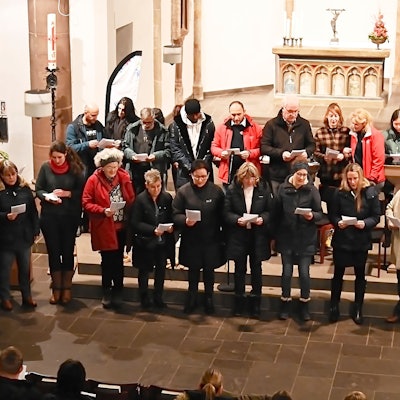 Sängerinnen und Sänger stehen gemeinsam im Altarraum der Kirche Marmagen und schauen auf Texthefte, die sie in den Händen halten.