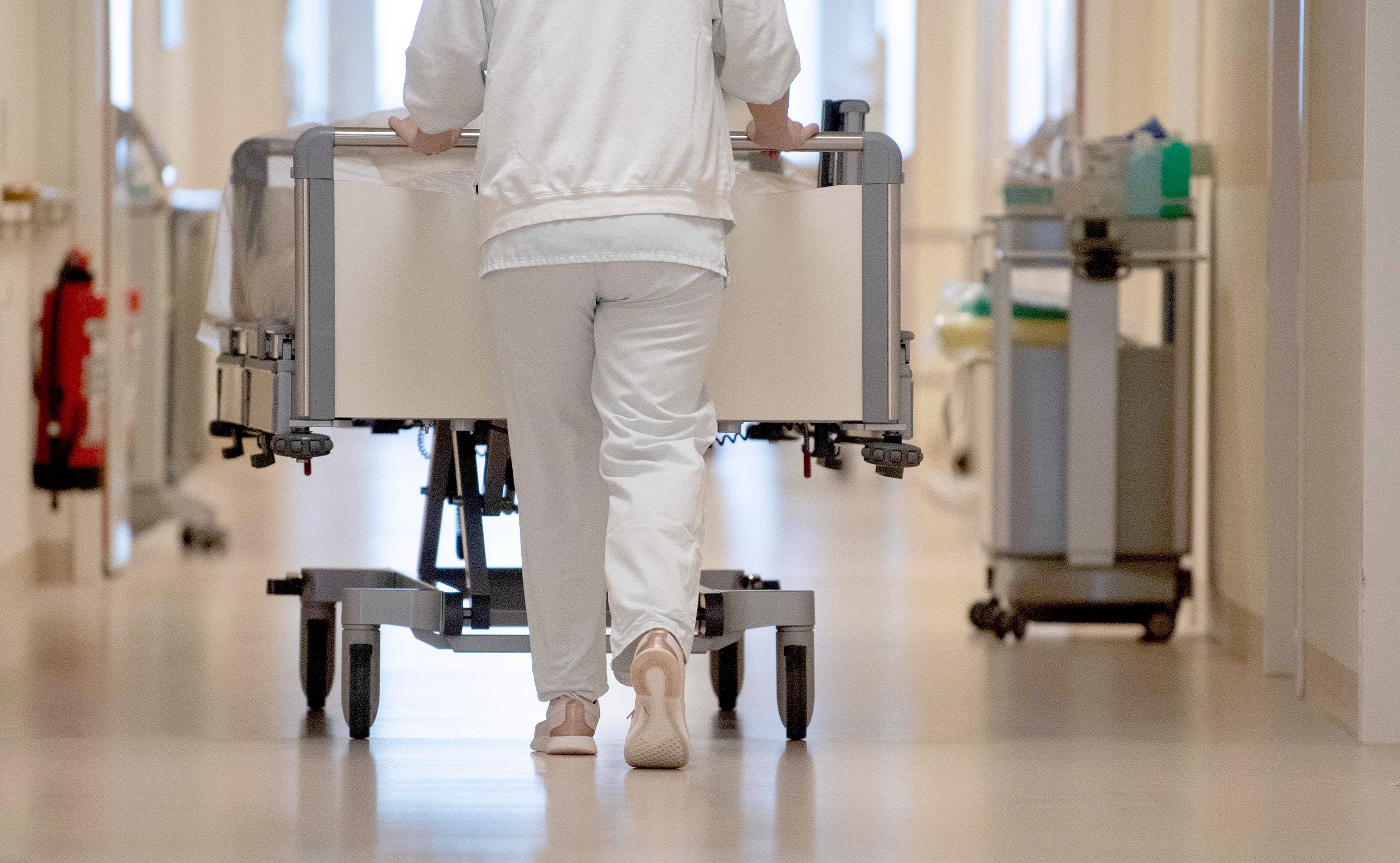 Eine Krankenpflegerin schiebt ein Krankenbett durch einen Krankenhausflur.