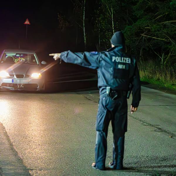 In der Dunkelheit rollt ein Auto auf einen Polizisten zu, der dem Fahrer mit energischem Handzeichen den Weg zur Kontrollstelle weist.