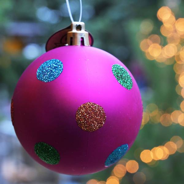 Eine bunte Tannengbaumkugel hängt vor einem mit einer Lichterkette geschmückten Weihnachtsbaum. Foto: Michael Bahlo/dpa +++ dpa-Bildfunk +++