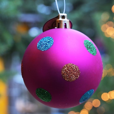 Eine bunte Tannengbaumkugel hängt vor einem mit einer Lichterkette geschmückten Weihnachtsbaum.  Foto: Michael Bahlo/dpa +++ dpa-Bildfunk +++