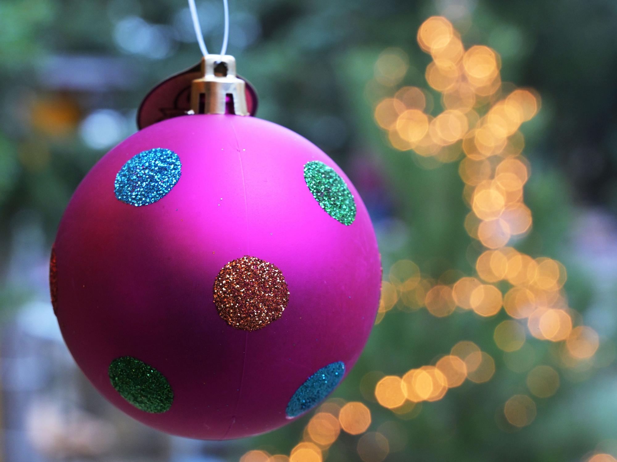 Eine bunte Tannengbaumkugel hängt vor einem mit einer Lichterkette geschmückten Weihnachtsbaum. Foto: Michael Bahlo/dpa +++ dpa-Bildfunk +++