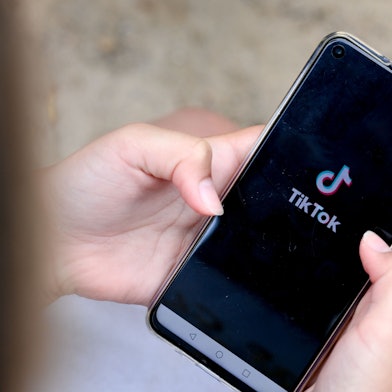 Ein Mädchen hält ein Smartphone in den Händen, auf dem das Logo von TikTok zu sehen ist.