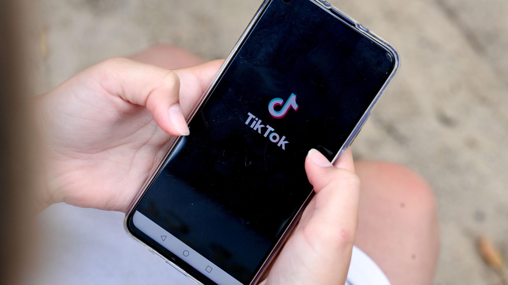 Ein Mädchen hält ein Smartphone in den Händen, auf dem das Logo von TikTok zu sehen ist.